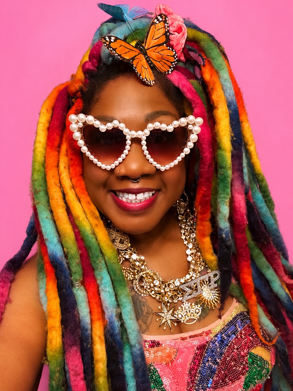 Melissa Rogers wearing rainbow locs, pearl heart sunglasses, layered statement jewelry and a colorful top